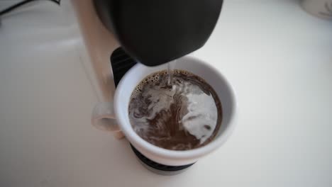 cup of coffee being filed by coffee machine close up in slow motion