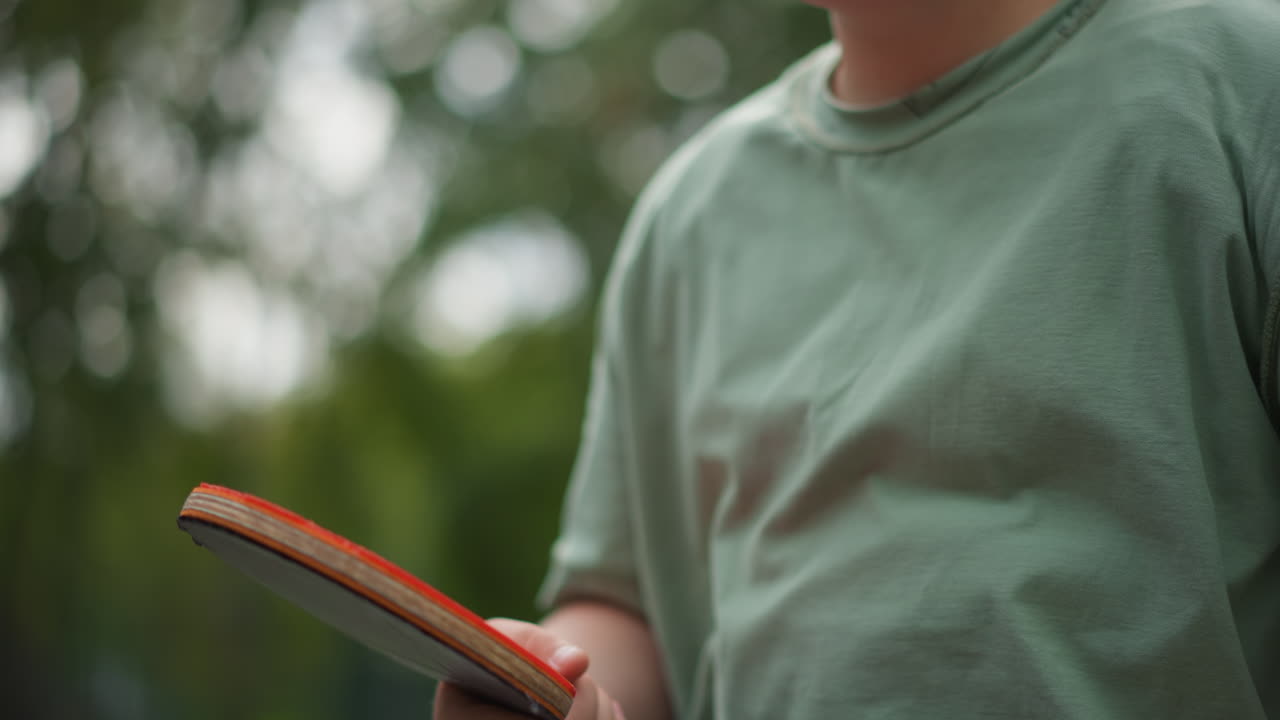 Player In Green Shirt Practices Outdoors, Casual Summer Training With Youth Adjusting Paddle Outdoors In Focus, Youthful Player In Green Shirt Practices Gently With Paddle In Outdoor Summer Setting