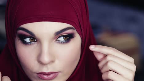 Unbelievably-beautiful-girl-with-hazelnut-eyes-and-purple-hijab-on-her-head-is-adjusting-her-traditional-arabic-head-cover-while-cheking-out-her-flawless-make-up