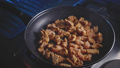 mixing floured and seasoned pieces of chicken in a frying pan using a wooden spoon, close up view