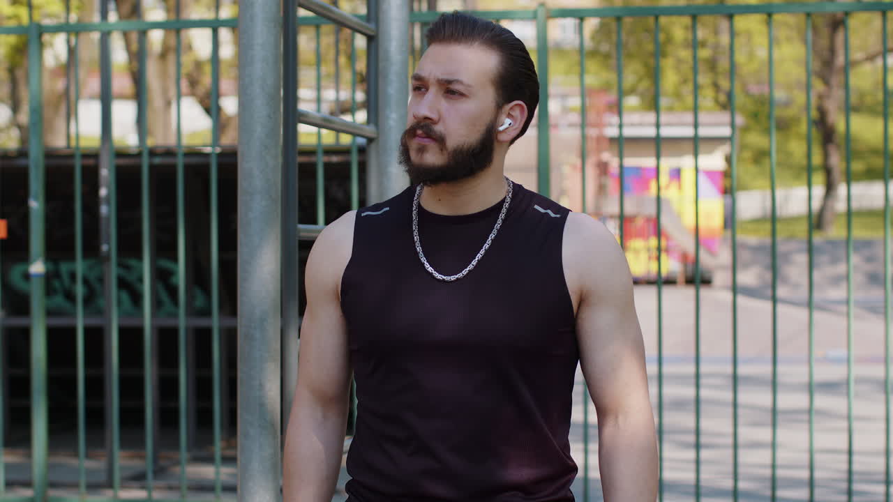 Athletic lebanese man in sportswear enjoying listening to music in earphones from smartphone app