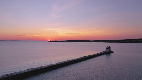 flying along a snow covered rocky breakwater towards the lighthouse at the end while the sun just crests over the horizon