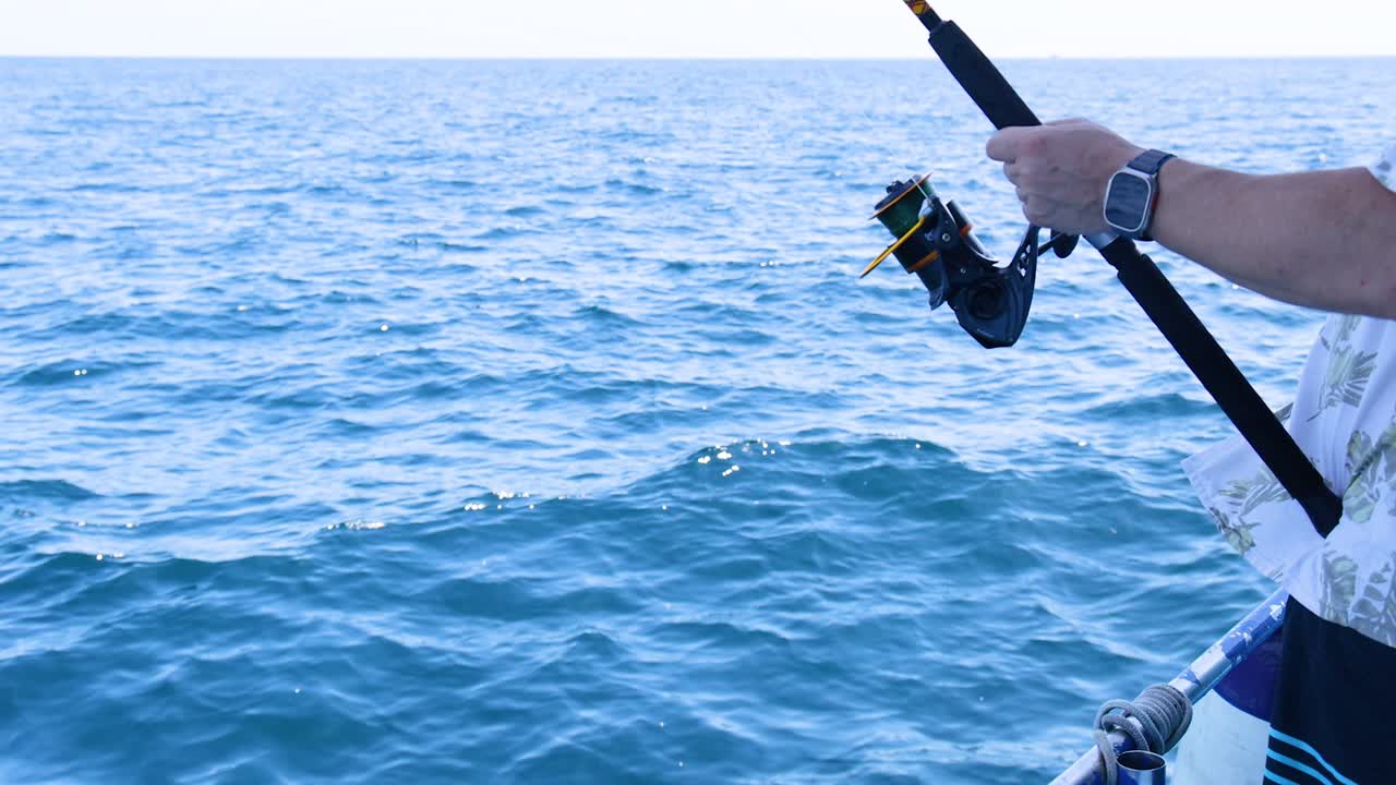 A person fishing from a boat in Phuket, Thailand, under bright daylight. The video captures serene ocean views and focused angling