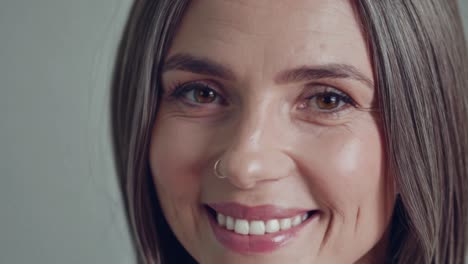 a person expresses joy and warmth through a genuine smile, showcasing positive emotions in a neutral background. the close-up highlights their engaging and friendly demeanor.