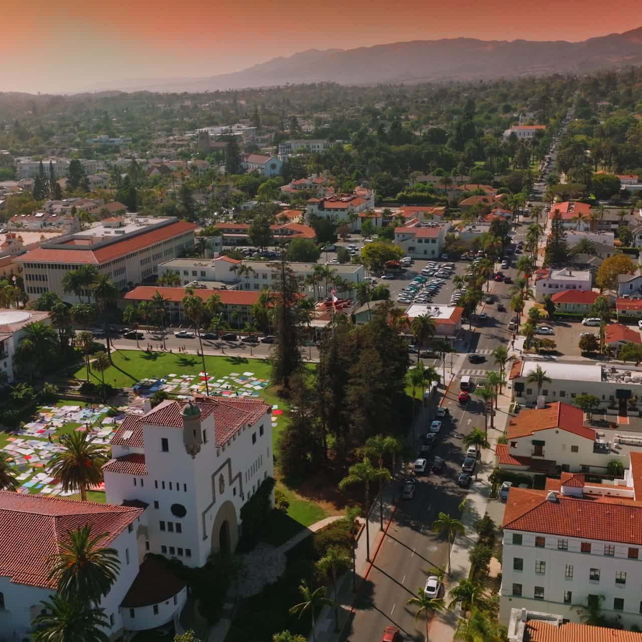 Lovely white houses with orange roofs, numerous cars on the streets and parking lots. Beautiful architecture and hills of Santa Barbara at backdrop of pink skies