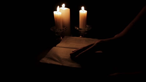 turning the pages of holy book lit by candle light in a hidden, dark place