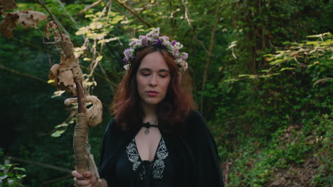 young druid girl walks and sits in a forest contemplating her wooden staff medium shot