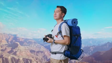 Side View Of Asian Male Hiker With Mountaineering Backpack Smiling And Holding A Camera In His Hands Then Looking Around While Traveling At The Top Of Mountain