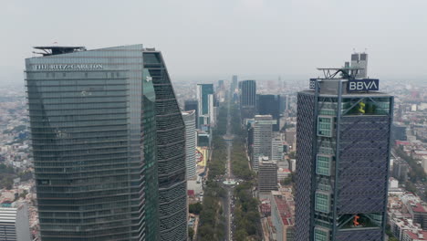 Tilt-down-reveal-shot-of-wide-long-straight-street-leading-between-modern-tall-office-buildings.-Aerial-view-of-cityscape.-Mexico-City,-Mexico.