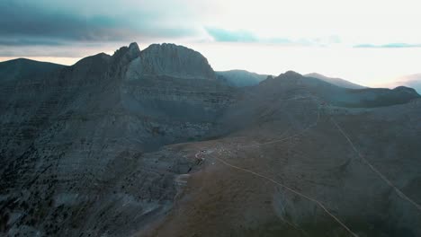 establishing wide aerial shot of mountain olympus reveals a hut with campers and tents on the valley while the sun sets and the clouds cover it