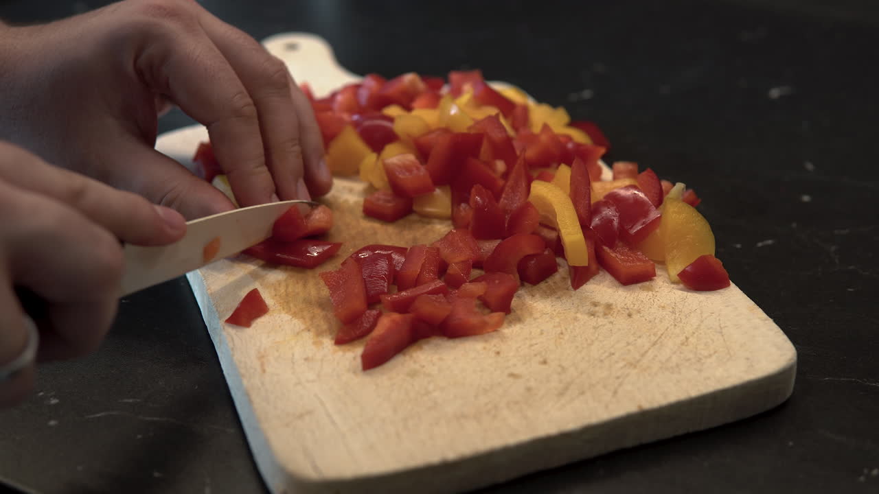 A man slices coloured peppers on a wooden board, close up