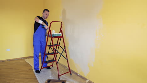 young man in overalls renovating room in the house. painter worker using a paint roller doing makeover of a room. room decoration with new color.