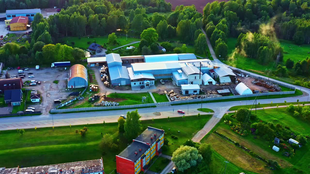 Aerial view of industrial complex with warehouses and smoke rising with golden hour sunlight