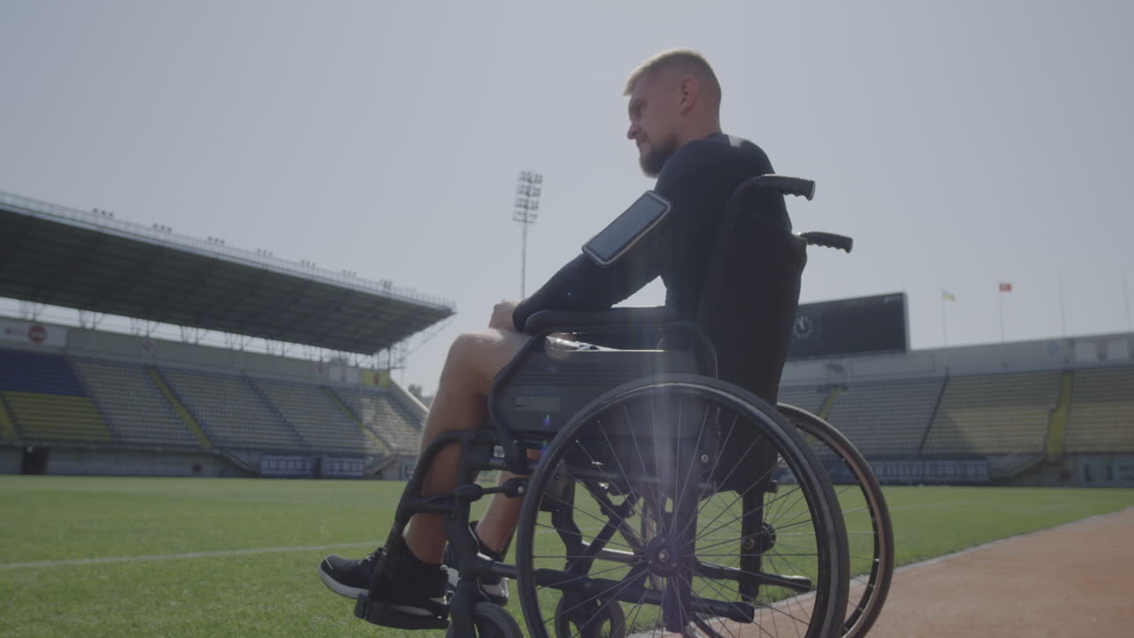 Disabled Athlete Sitting in Wheelchair by a Sports Field Medium Shot of a Sad Disabled Athlete Sitting in his Wheel Chair by a Sports Field and Looking Away