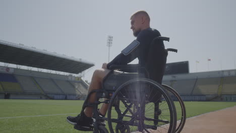 disabled athlete sitting in wheelchair by a sports field medium shot of a sad disabled athlete sitting in his wheel chair by a sports field and looking away