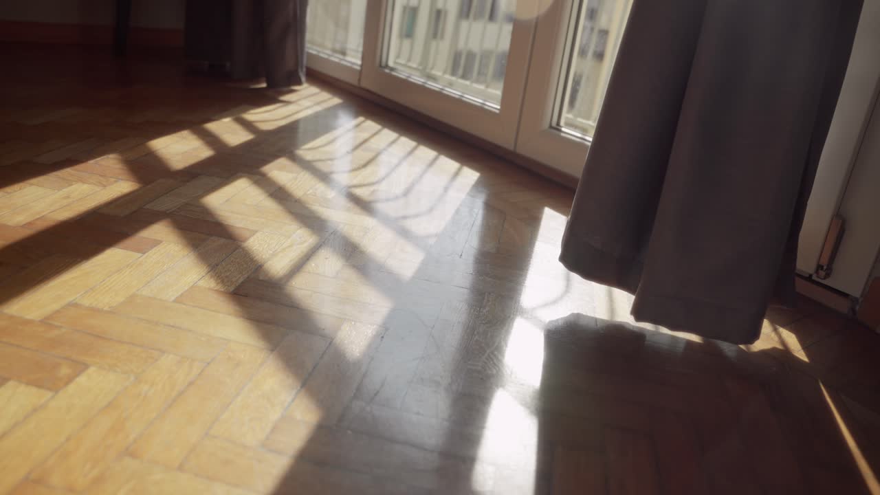 Shadows of sunlight entering from balcony window in apartment during daytime. Beautiful sun shining through as camera pulls away. Bedroom or hotel in early morning. Parquet floor inside European room