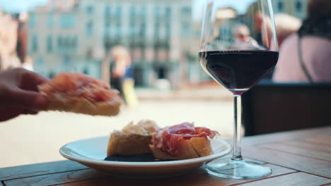 primer plano de una persona comiendo pan de focaccia italiano con jamón crudo y vino tinto durante el día soleado en venecia, italia