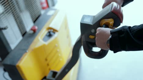 hands on the control lever of a hydraulic stacker. a worker lifts loads in a warehouse. close-up