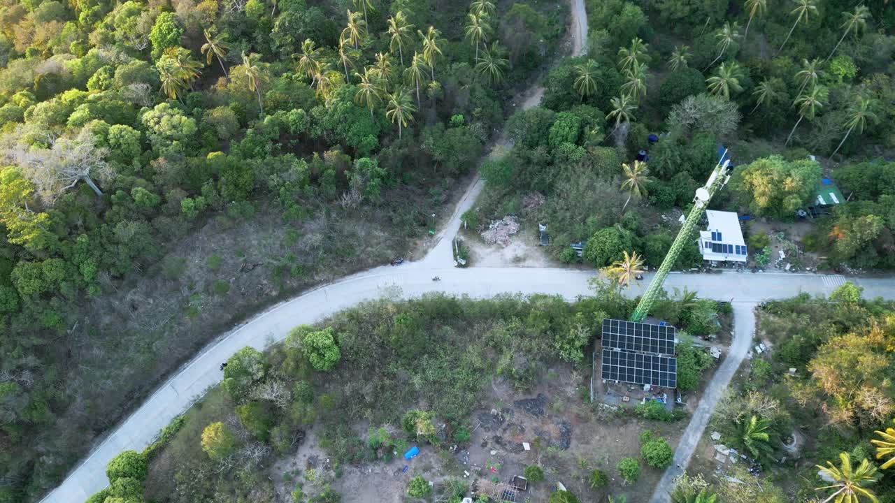 Scooter kører ad smal landevej med solcelleanlæg for grøn energi i naturen med palmetræ, luftfoto oppefra
