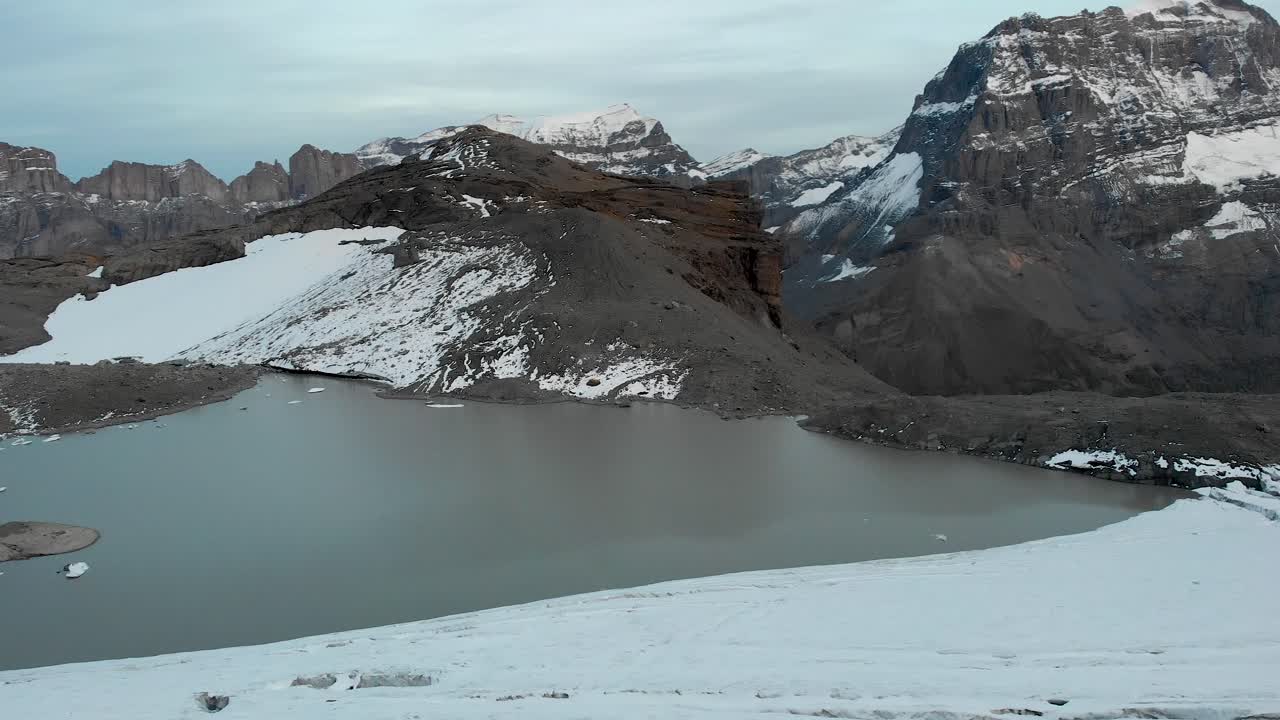 Aerial flyover over the glacial lake and ice of the Claridenfirn glacier in Uri, Swizerland with a spinning view of the mountain peaks of Klausenpass such as T&ouml;di