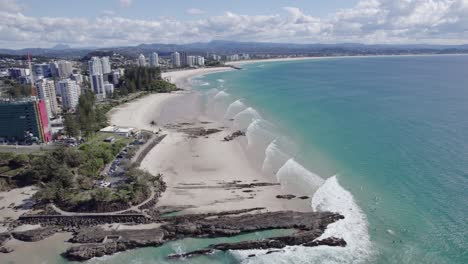 Vista-Aérea-Del-Parque-Oceánico-Con-Vista-A-La-Roca-Cerca-De-Las-Rocas-De-Pargo-Y-El-Bar-Del-Club-De-Surf-De-La-Bahía-Del-Arco-Iris-En-Coolangatta,-Queensland,-Australia