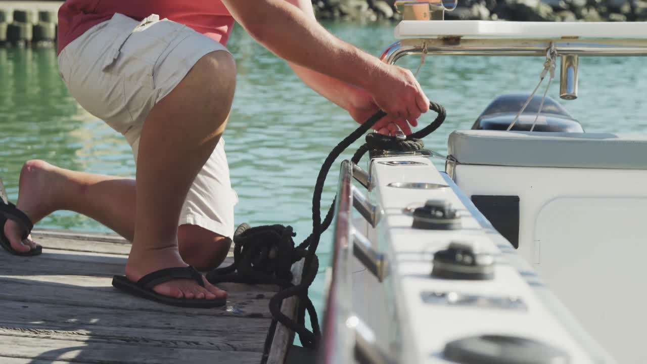 Side view low section of a Caucasian man untying a rope on the boat harbor side