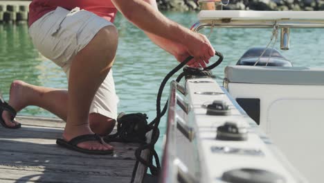 Vista-Lateral-De-La-Sección-Baja-De-Un-Hombre-Caucásico-Desatando-Una-Cuerda-En-El-Lado-Del-Puerto-Del-Barco