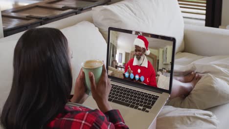 Mixed-race-woman-on-laptop-video-chat-having-coffee-during-christmas-at-home