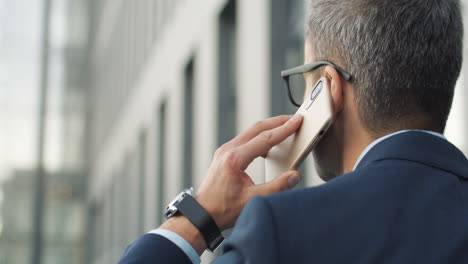 rear view of grey haired businessman talking on phone while walking the street