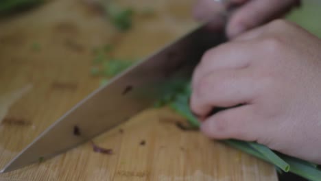 closeup on a woman chopping spring onions on a wooden kitchen table