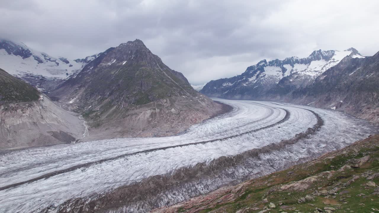 A poignant 4K aerial view of the Aletsch Glacier, highlighting the thinning ice and prominent debris bands that signal rapid glacial retreat and the environmental impact of climate change in the Swiss