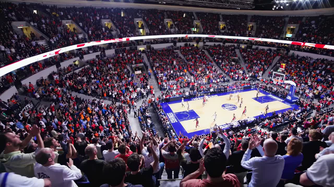 Ripresa video dall'alto di un'arena da basket gremita, che cattura l'energia dei tifosi esultanti e luminosi.