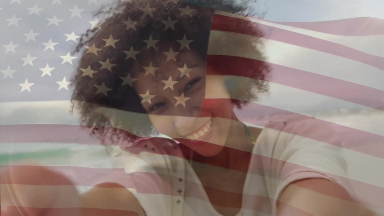 Giovane donna felice con i capelli ricci che sorride con una sovrapposizione di bandiera americana che sventola.