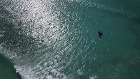 Aerial-overhead-flight-showing-kite-surfer-surfing-on-clear-Pacific-Ocean,jumping-and-falling-on-waves-during-beautiful-weather-outside