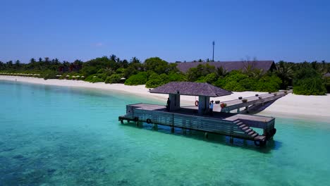 Man-waiting-for-boat-on-Maldives-wooden-pier,-Aerial-pan-around-tranquil-sea-4k