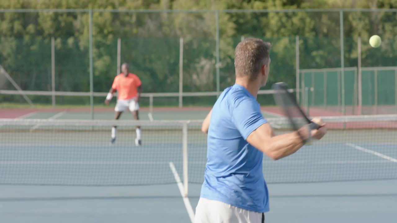 Diverse male tennis players playing tennis on outdoor court in slow motion