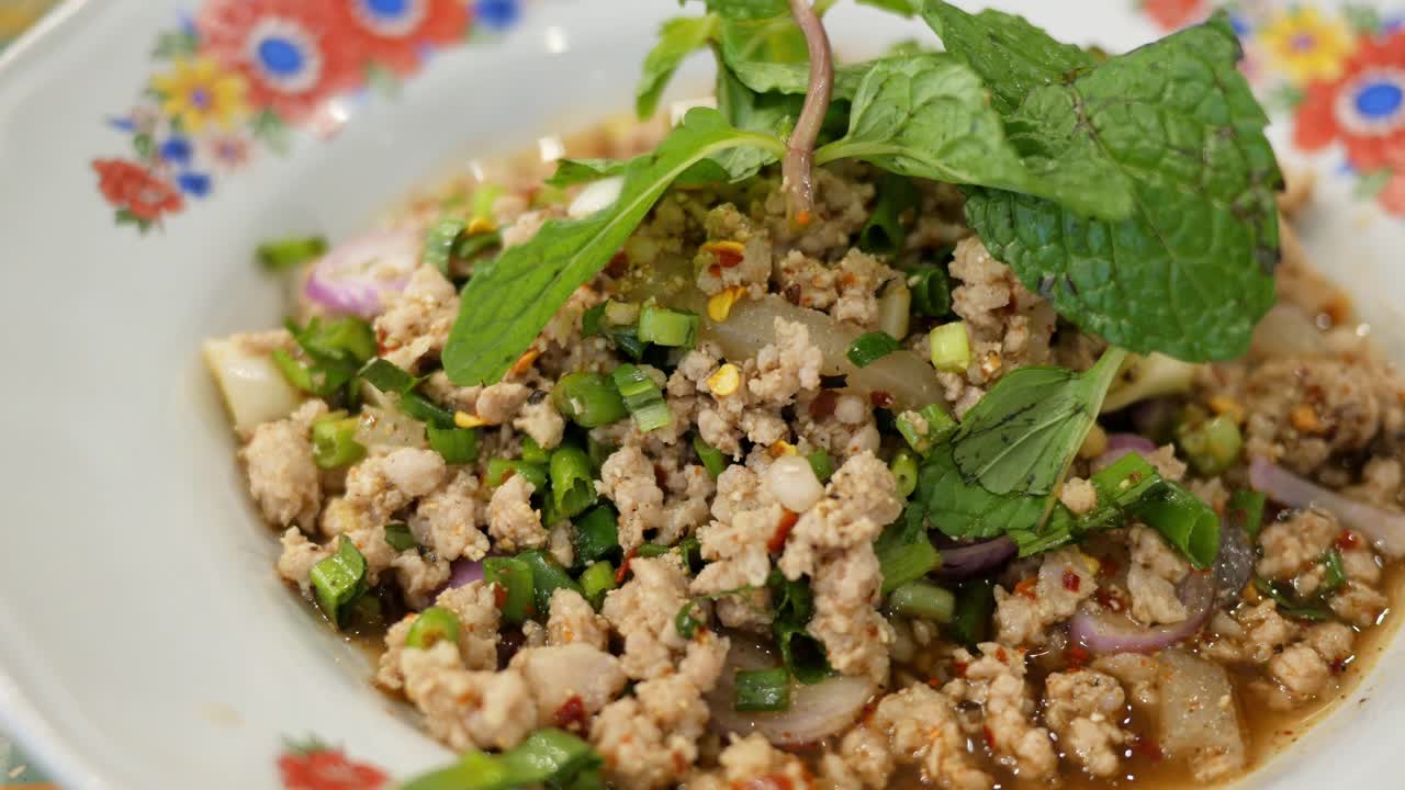 cerca de un plato lleno de una popular comida tailandesa de isan llamada larb, una mezcla de pollo picado, menta, pimienta, cilantro, lima y salsa de pescado