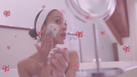 Animation-of-floral-hearts-over-smiling-african-american-mother-and-daughter-pampering-in-bathroom