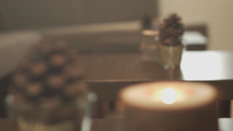 close up of a modern design wooden candle and a pinecone on a table in a hotel lobby with a wooden table with another candle and a pinecone in the background