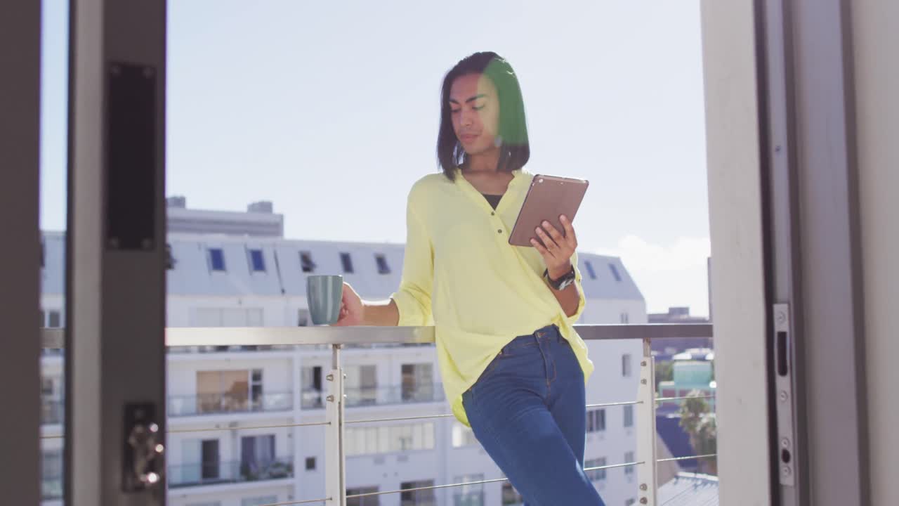 persona de género fluido de raza mixta bebiendo una taza de café y usando una tableta en la terraza del techo