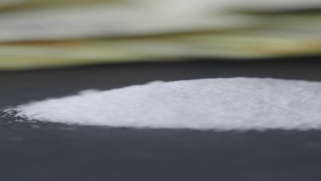 pila de polvo blanco en una superficie oscura con dinero borroso en el fondo