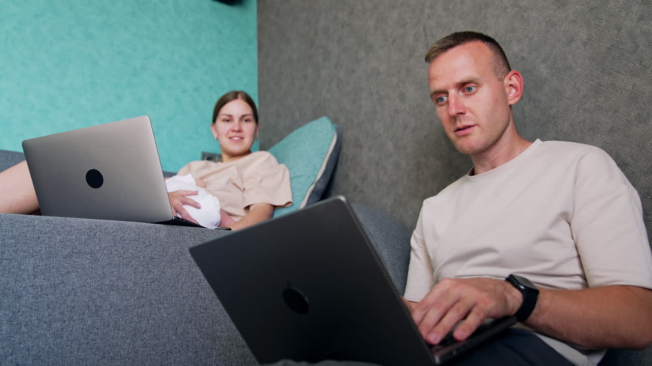Caucasian man looks intently on laptop screen. Working first time parents combining work and baby care.