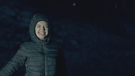 smiling young woman jumps and enjoys heavy rain at night