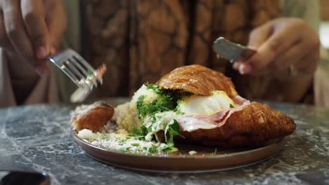 woman enjoying delicious croissant eggs benedict for breakfast