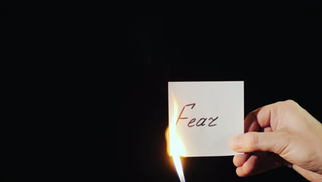 man burns a paper with the inscription fear