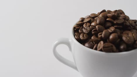 video de una taza de granos de café marrón tostados sobre un fondo blanco
