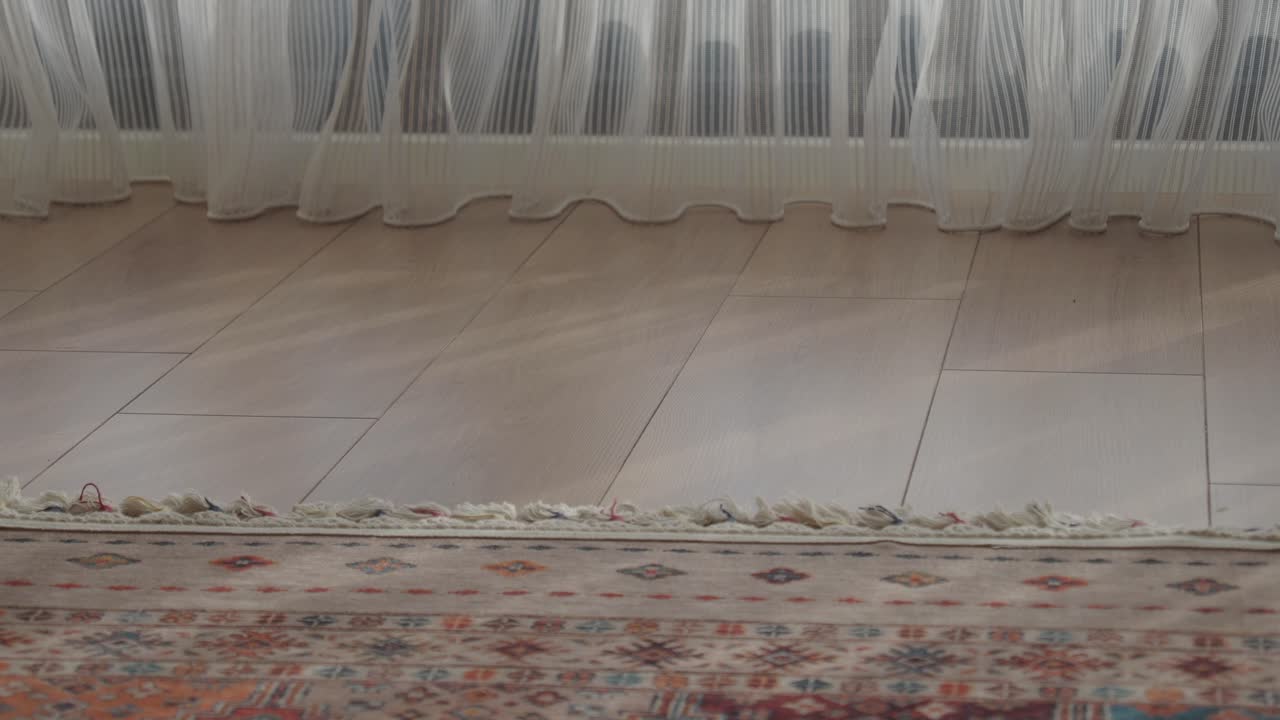 Closeup of a rug on a wooden floor with a white curtain in the background