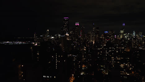 Aerial-drone-backward-moving-shot-along-the-multiple-high-rise-buildings-in-congested-downtown-area-of-Chicago,USA-at-night-time
