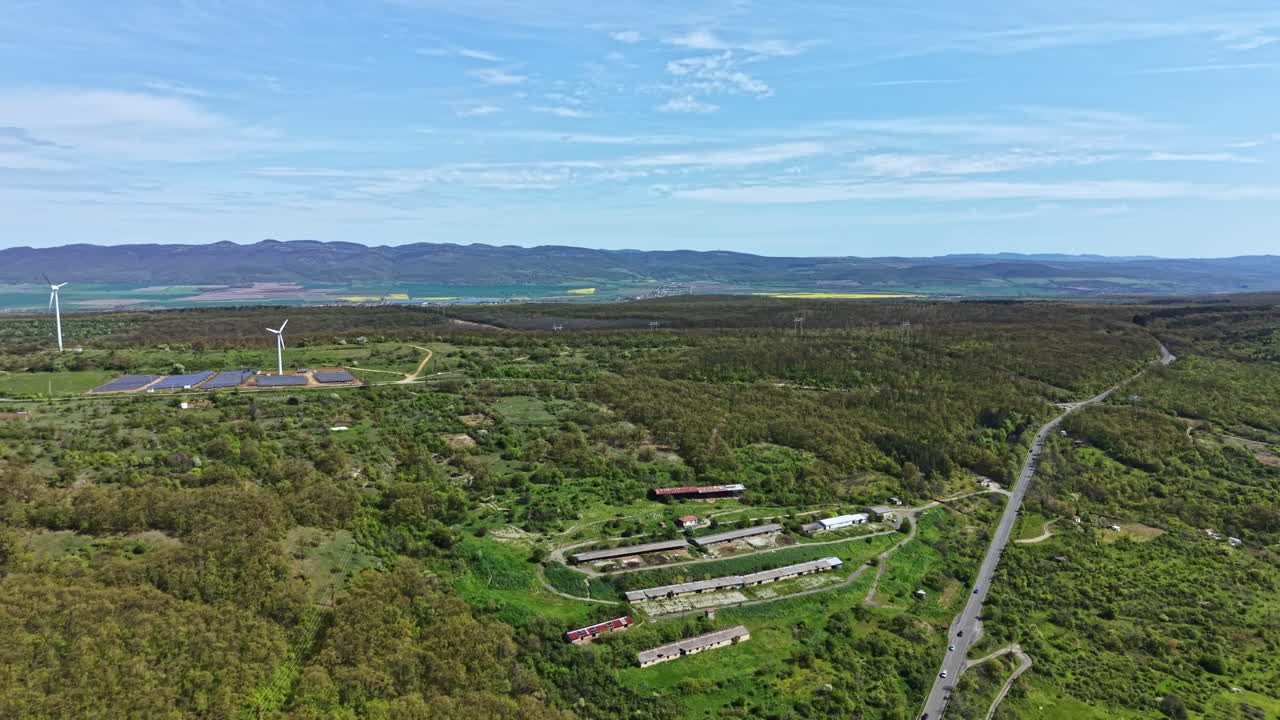 Aerial view of wind turbines and farmland in a green valley during daytime with clear sky and distant mountains