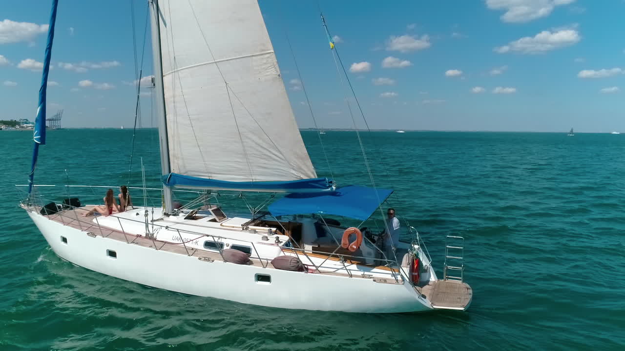 Beautiful white boat with sails on water. Modern yacht floating among many others on sea. People rest on a sea voyage during a sail ship in summer.